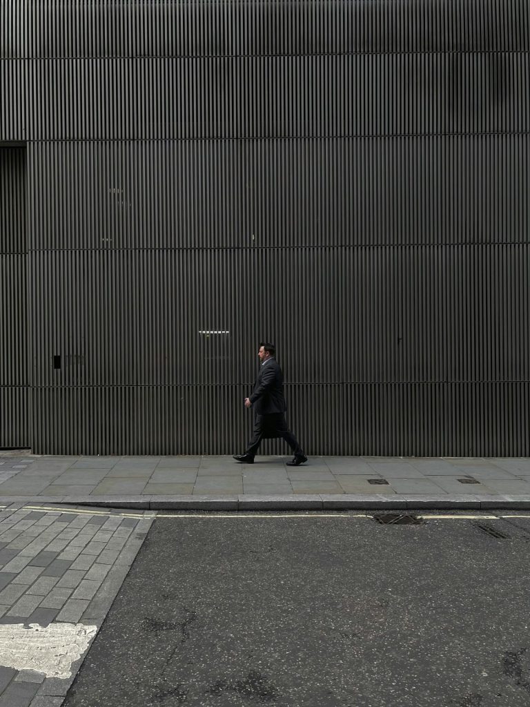 gehender Mann im schwarzen Anzug vor einem großen Gebäude, als Symbol für einen Unternehmer, der von der Körperschaftssteuer-Senkung betroffen sein könnte